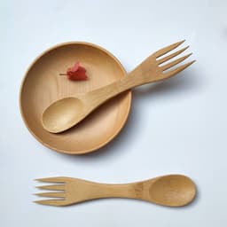 A bamboo spoon and fork set in a wooden plate, featuring a natural finish and a small decorative item.