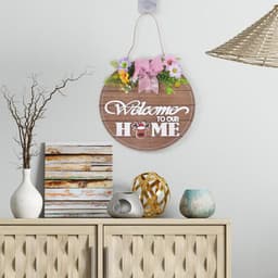 A round wooden door hanger featuring a floral design and the phrase "Welcome to our Home" in white lettering.