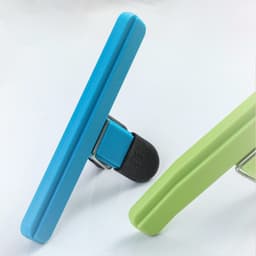 A large chip bag clip in blue and green, featuring a spring-loaded design and a rubberised grip. It has a logo.