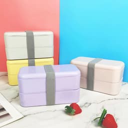 Double layer lunch boxes in pastel colours: grey, yellow, lavender, and pink, secured with grey straps on a marble surface.