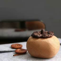 Persimmon-shaped aroma diffuser in natural wood with a brown top. Includes wooden buttons nearby.