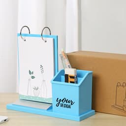 A blue desk pen holder with a calendar and a holder for pens, placed on a wooden surface next to a box.