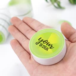 A hand holds a circular, green disposable compressed towel with a white rim and a design placeholder on top.