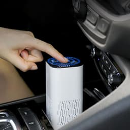 A white mini portable air purifier with a blue top, placed in a vehicle's centre console.