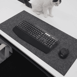 A large grey felt desk pad with a keyboard and mouse on a white desk, accompanied by a cat in the background.