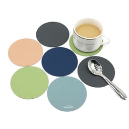 A coffee cup on a green silicone coaster surrounded by six coloured coasters in peach, navy, green, blue, and grey.