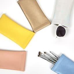 A collection of assorted pouches in yellow, gold, pink, and blue, alongside a pair of sunglasses and some brushes.