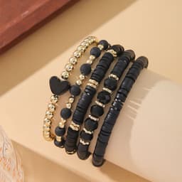 A stack of clay bead bracelets featuring black and gold colours, including one with a heart-shaped bead.