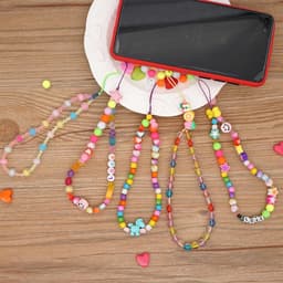 A set of colourful beaded mobile phone charms in various designs, placed next to a smartphone on a plate.