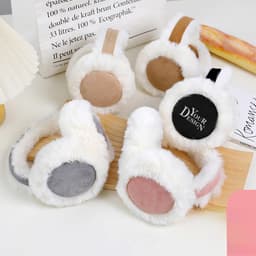 A set of personalised winter earmuffs in white with pink, grey, and brown accents on a wooden surface.