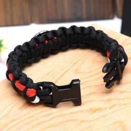 A black and red woven paracord bracelet with a black clasp, resting on a wooden surface.