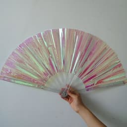 A hand holding a large, pink and iridescent PVC folding fan with a transparent handle.