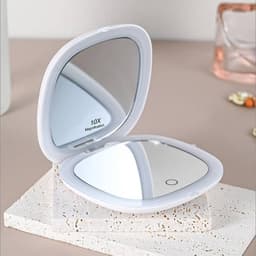 A white portable folding LED mirror with a magnification feature, resting on a textured surface.