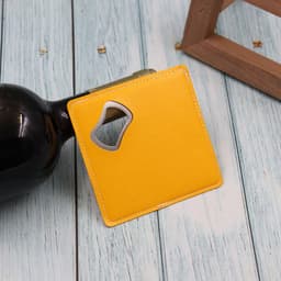 A drink bottle opener coaster in bright yellow, featuring a metal bottle opener cutout, placed on a wooden surface.