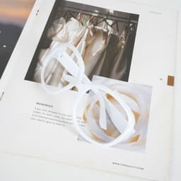 An oversized vintage eyeglasses frame in white, placed on a magazine featuring a soft floral image.