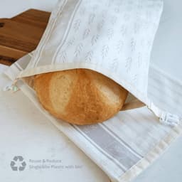 A reusable storage bag in light colour with a loaf of bread inside, featuring a logo on the side.
