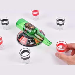 A green drink bottle resting on a game base, surrounded by clear shot glasses in red and black.