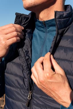 A navy puffer vest being worn, with a person adjusting the zip, layered over a blue top.
