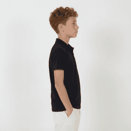 A side view of a youth wearing a black polo shirt paired with white trousers. The shirt has a branded logo.