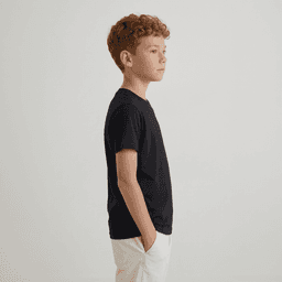 A child stands in profile wearing a black essential tee and white shorts, with hands in pockets.