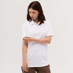 A woman wearing a white polo shirt, looking at her sleeve, set against a plain background. The shirt features a logo.