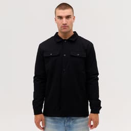 A black Studio Canvas Jacket features a collared design and front pockets, worn by a model against a plain background.