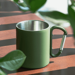 A green thermo mug with a stainless steel interior and a carabiner-style handle, resting on a wooden surface.