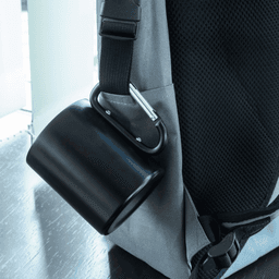 A black thermo mug attached to a grey backpack with a carabiner clip.