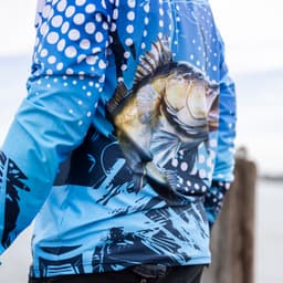 A blue long sleeve fishing tee with a fish graphic and abstract patterns, featuring a logo on the back.