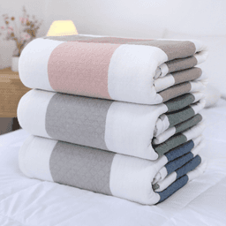 A stack of four blankets in soft hues of pink, grey, and navy, neatly folded on a bed. Each blanket features a patterned design.