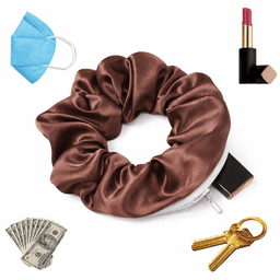 A brown satin scrunchie with a zipper, surrounded by a blue mask, lipstick, keys, and cash.