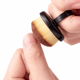 A makeup brush featuring soft bristles and a black handle, held by a hand with a thumb resting on the base.