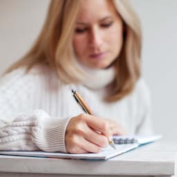 A bamboo pen is being held by a person who is writing in a notebook.