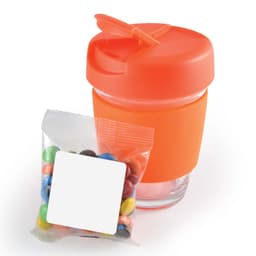 A reusable coffee cup in orange with a matching lid, accompanied by a bag of colorful M&M's.