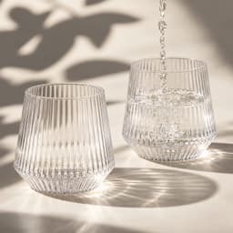 A drink bottle featuring a ribbed design, made of clear glass, with water being poured into two glasses.