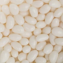A close-up of glossy white jelly beans scattered across a surface, with a branding logo visible.