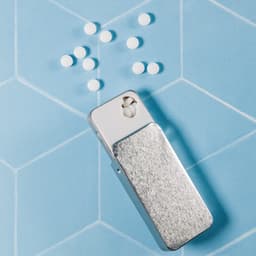 A silver slider tin filled with white sugar-free mints, placed on a blue hexagonal patterned background.