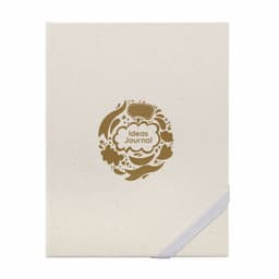 A cream-coloured journal with a gold decorative logo featuring floral designs and the words "Ideas Journal."