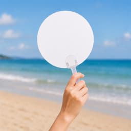 A handheld circular fan with a transparent handle against a beach backdrop and ocean waves.