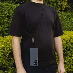 A person wearing a black shirt holds a smartphone attached to a black phone lanyard.