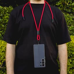 A phone lanyard in red with a grey phone attached, worn around the neck against a green background.