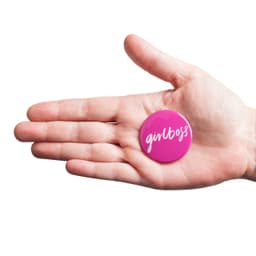A pink 45mm round badge held in a hand, featuring a logo or branding.