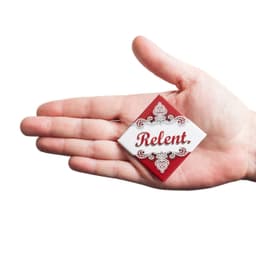 A hand holds a diamond-shaped badge featuring a red and white design with decorative elements and a logo.