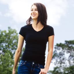 A black fitted t-shirt worn by a woman, outdoors with greenery in the background. The shirt has a v-neck design.