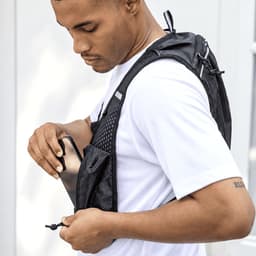 A black recycled running vest hydration pack being worn by a man, featuring mesh pockets for storage.