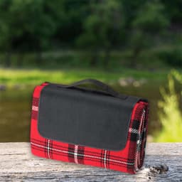 A red and black checked picnic rug with a black handle, resting on a wooden surface near water.