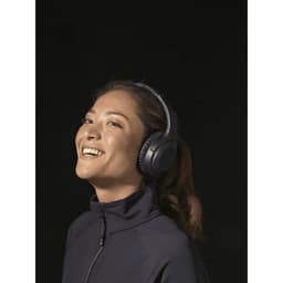 A woman wears black Anton ANC headphones, smiling against a dark background. The image features branding on the product.