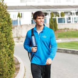 A blue quarter zip jumper for men, featuring a logo, worn by a smiling man walking outdoors.