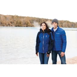 A man and woman wear jackets by a lakeside; the man's jacket is blue, while the woman's jacket is a mix of blue and black.