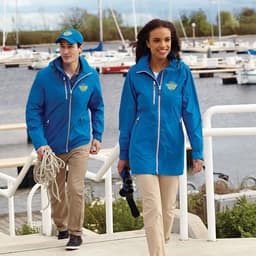 A blue rain jacket worn by a woman, paired with a blue cap and beige trousers, near a marina.